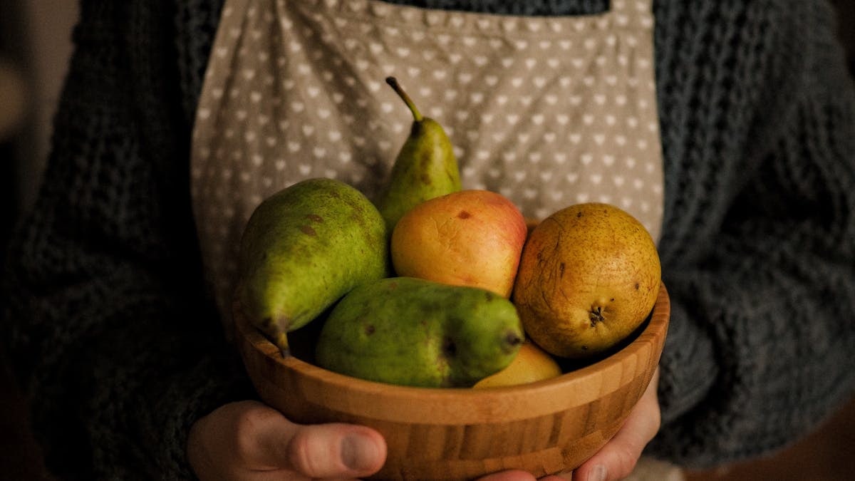 Close-up of a person holding a wooden bowl with fresh fruits including pears.